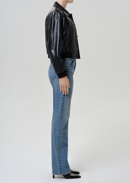 Woman wearing medium blue straight leg jeans with a black leather jacket viewed from the side on a grey background.