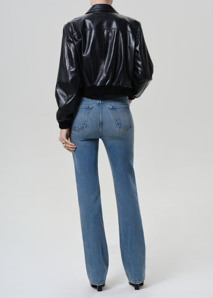 Woman wearing medium blue straight leg jeans with a black leather jacket viewed from the back on a grey background.