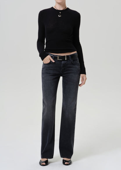 A model wearing a black long-sleeve cropped knit top, dark gray straight-leg jeans with a black belt, and black open-toe heels, standing against a light gray studio background.