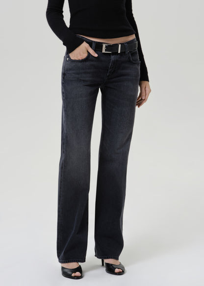 A model wearing a pair of dark charcoal gray wide-leg jeans with a black belt, paired with a black long-sleeve top and black heeled sandals, photographed against a light gray studio background.