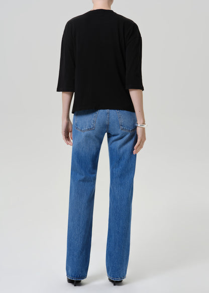 A model shown from the back wearing a black three-quarter sleeve top and blue straight-leg jeans against a light gray studio background.