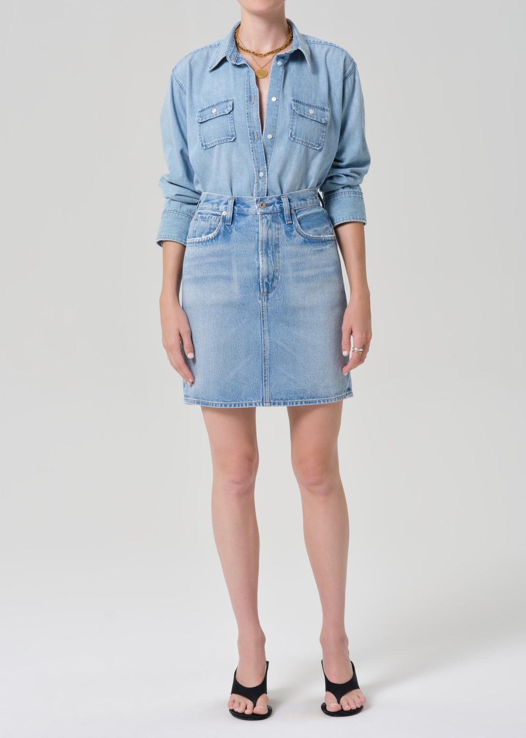 Person wearing a denim shirt and skirt with a grey background