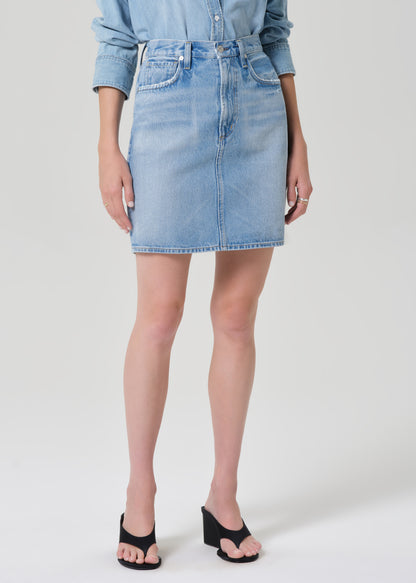 Person wearing a light blue denim skirt on a plain background