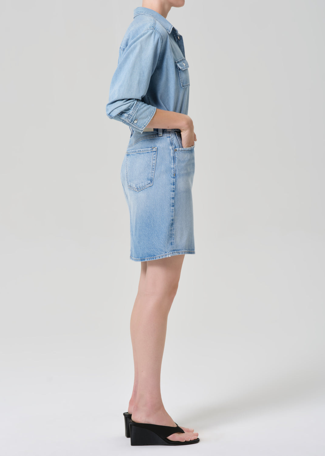 Person wearing a light blue denim skirt on a grey background