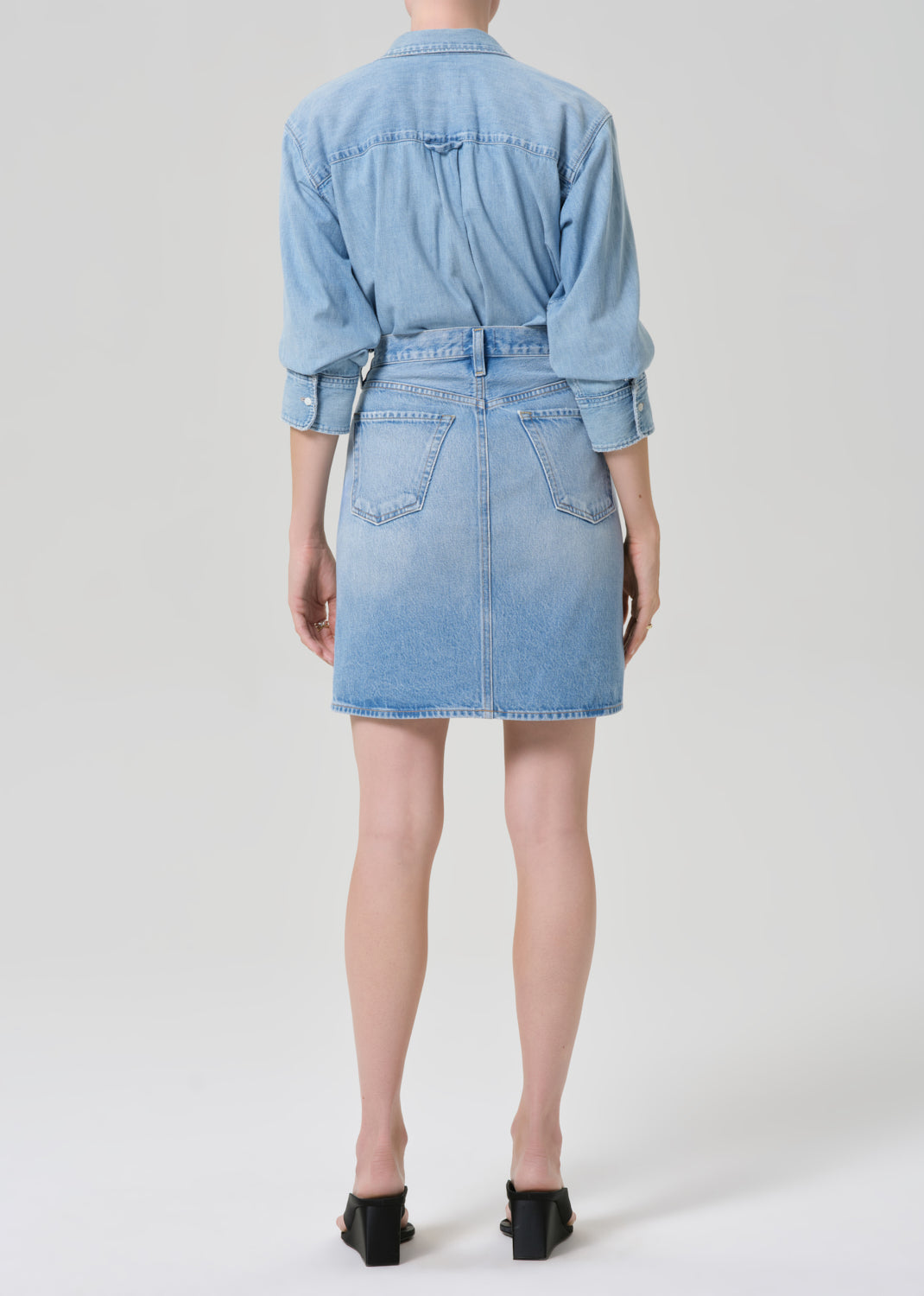 Person wearing a denim shirt and skirt with a grey background