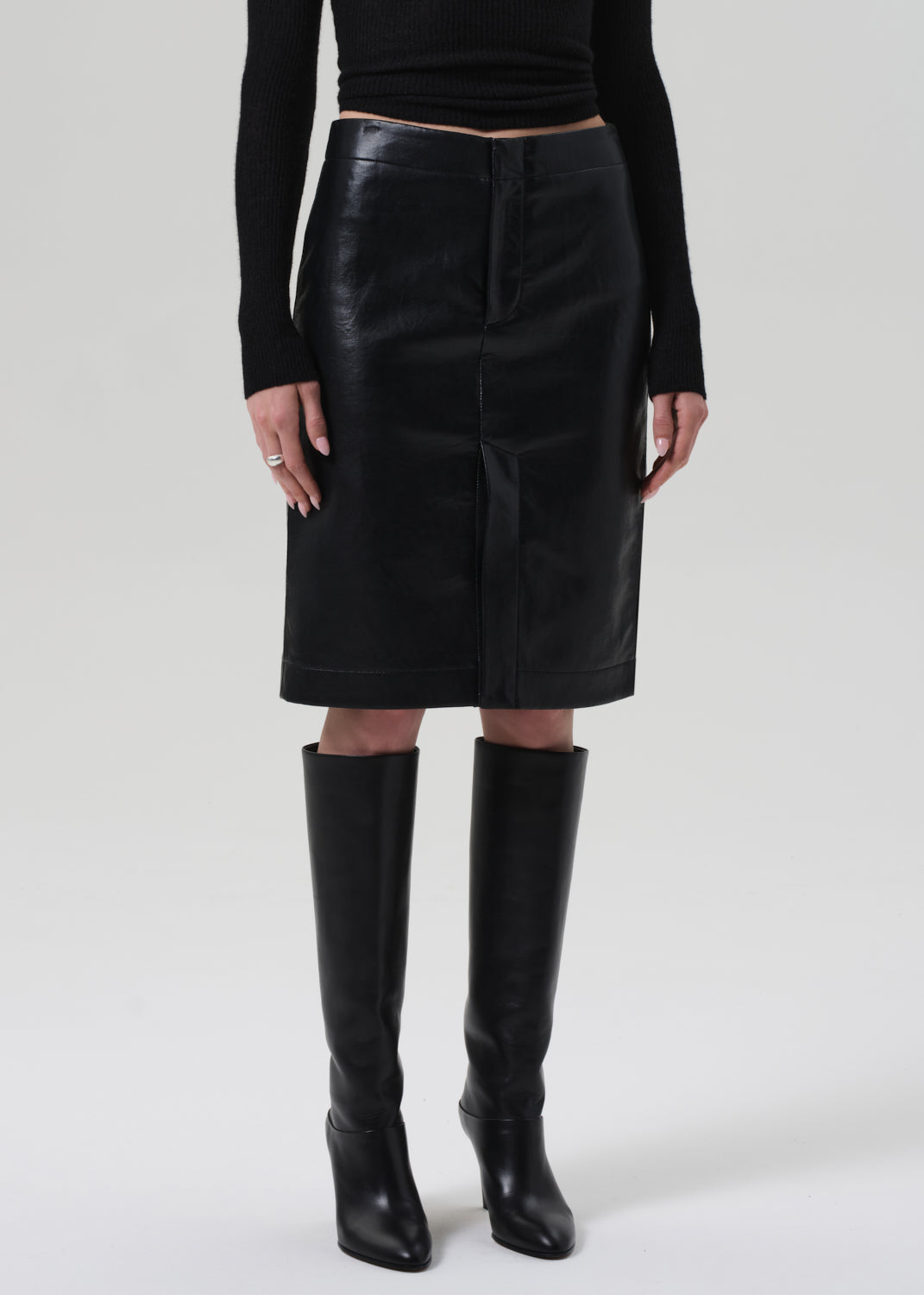 Person wearing a black leather skirt and black knee-high boots on a grey background