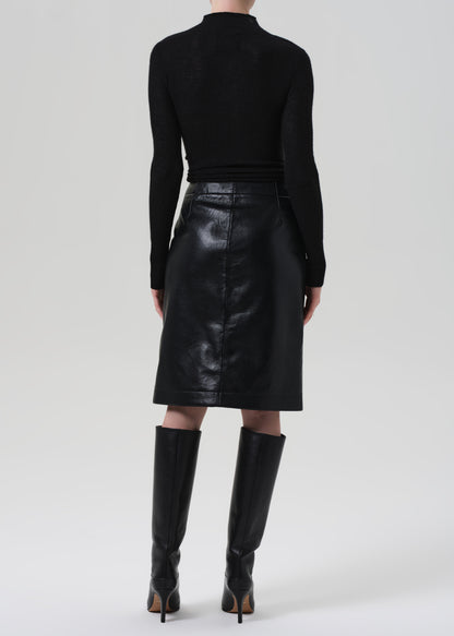 Person wearing a black leather skirt and black knee-high boots on a grey background