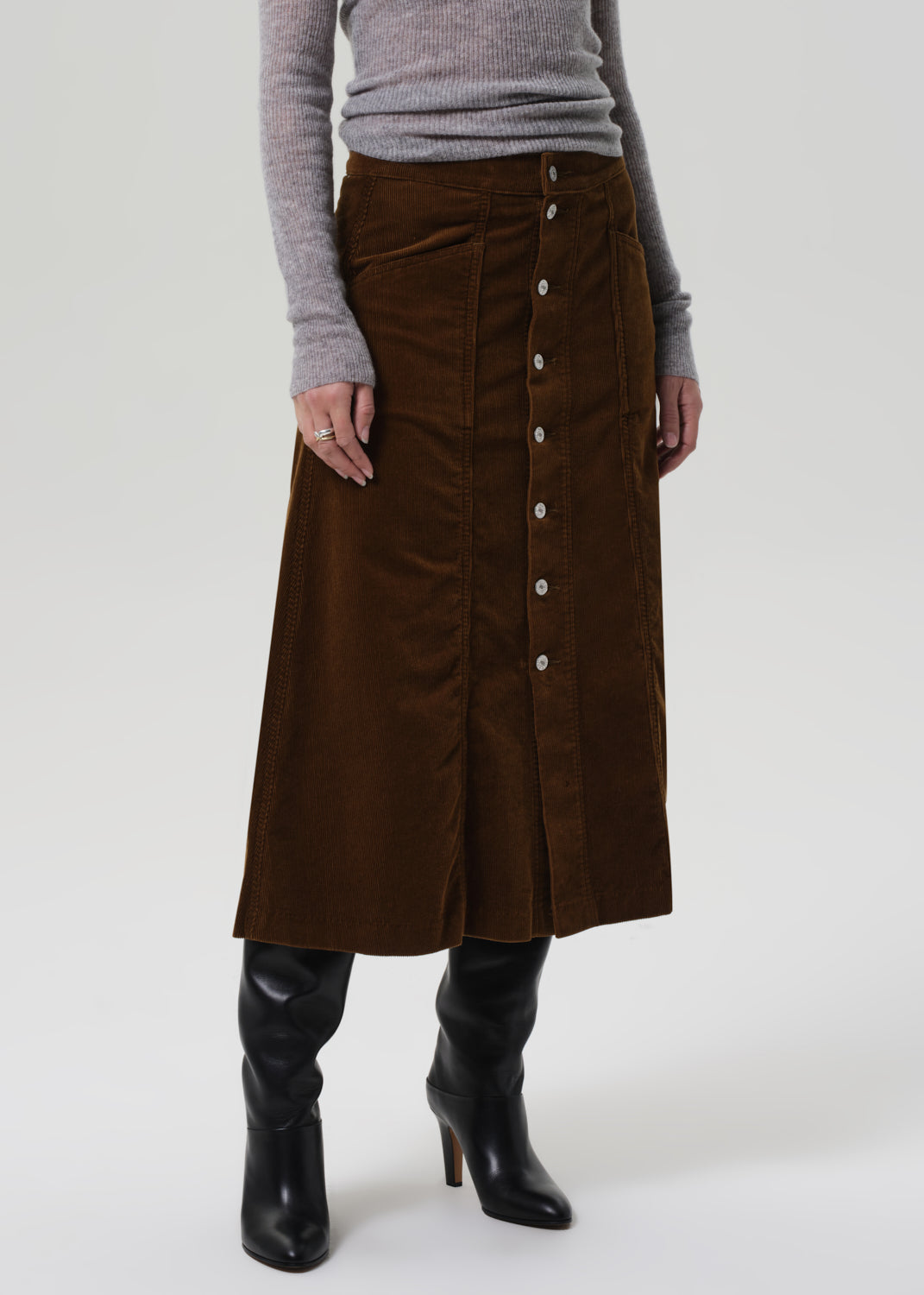 Person wearing a brown skirt and gray sweater on a grey background