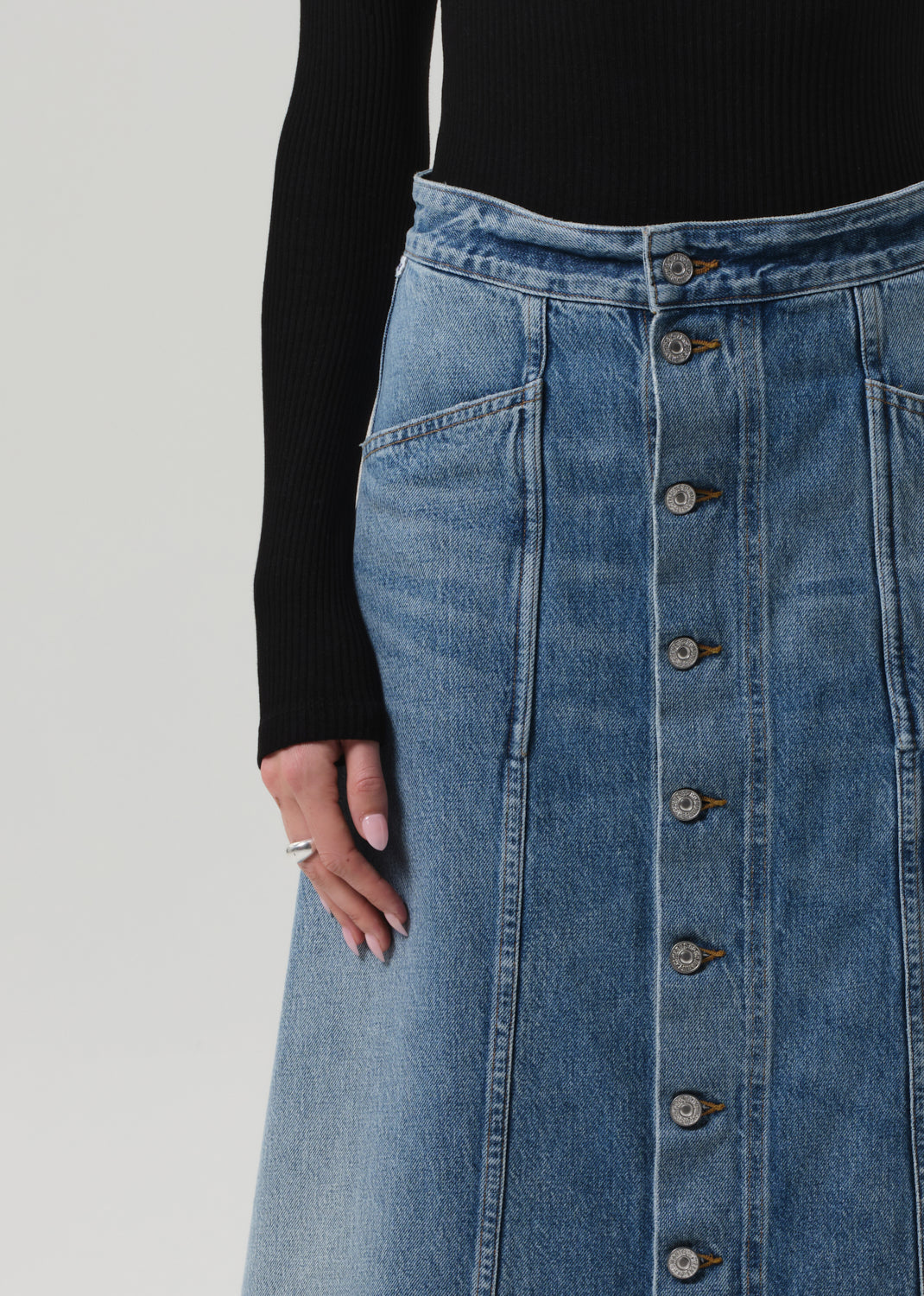 Person wearing a black turtleneck and blue denim skirt on a grey background