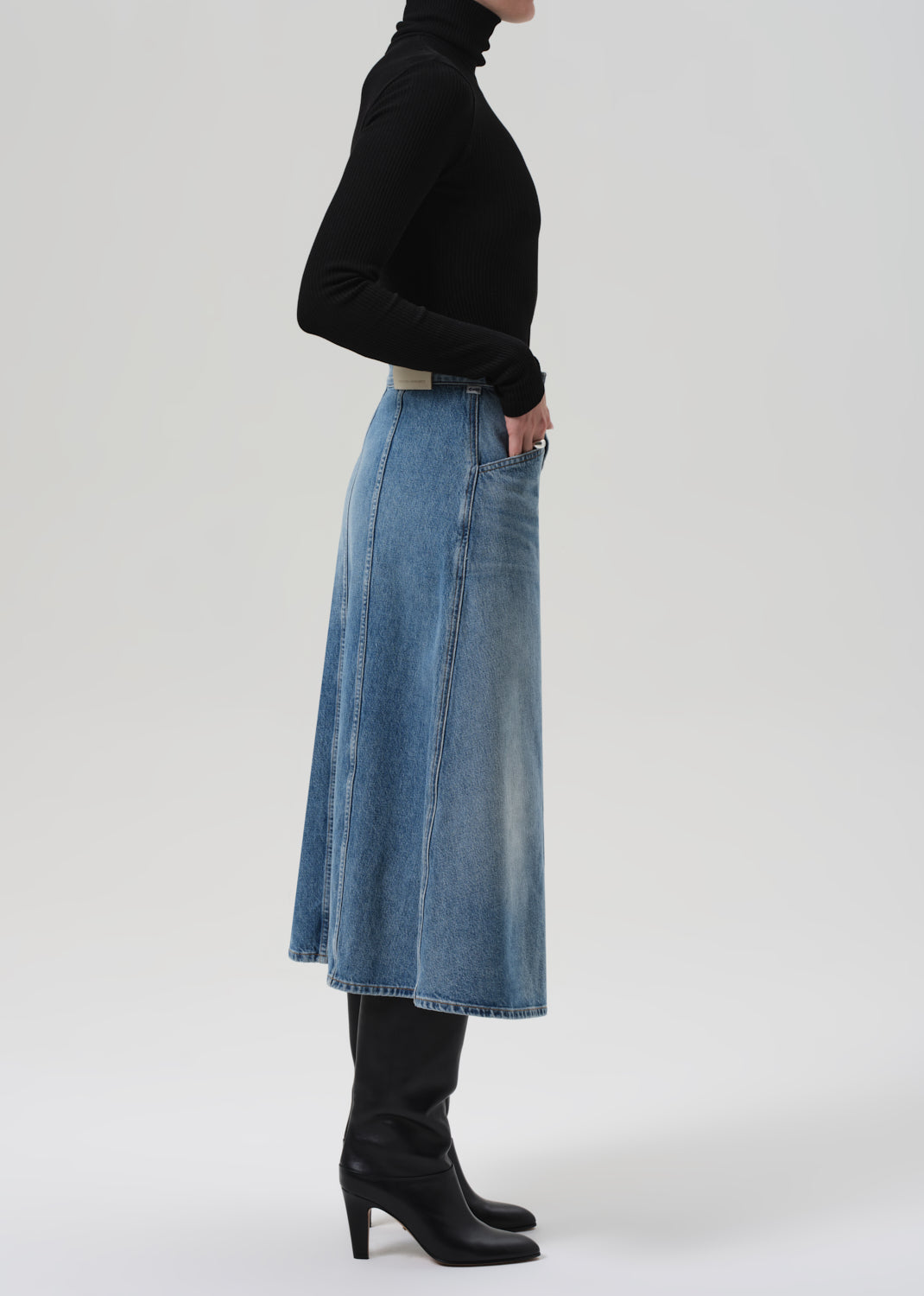 Person wearing a black turtleneck and blue denim skirt on a grey background