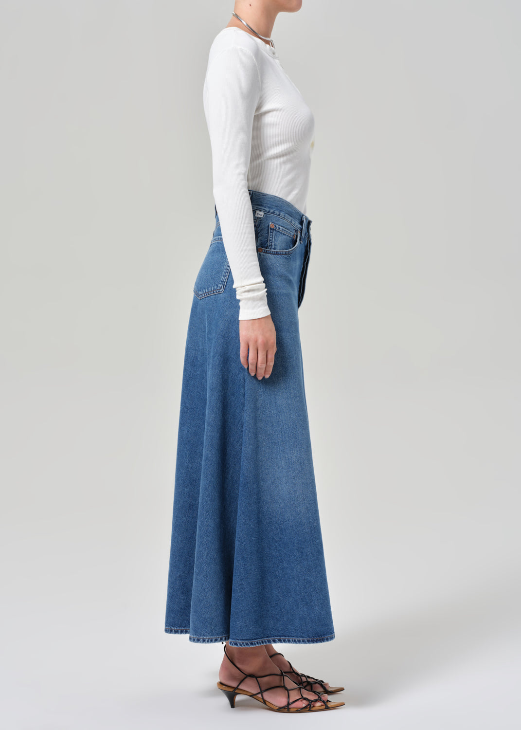 Person wearing a long blue denim skirt and white top on a plain background