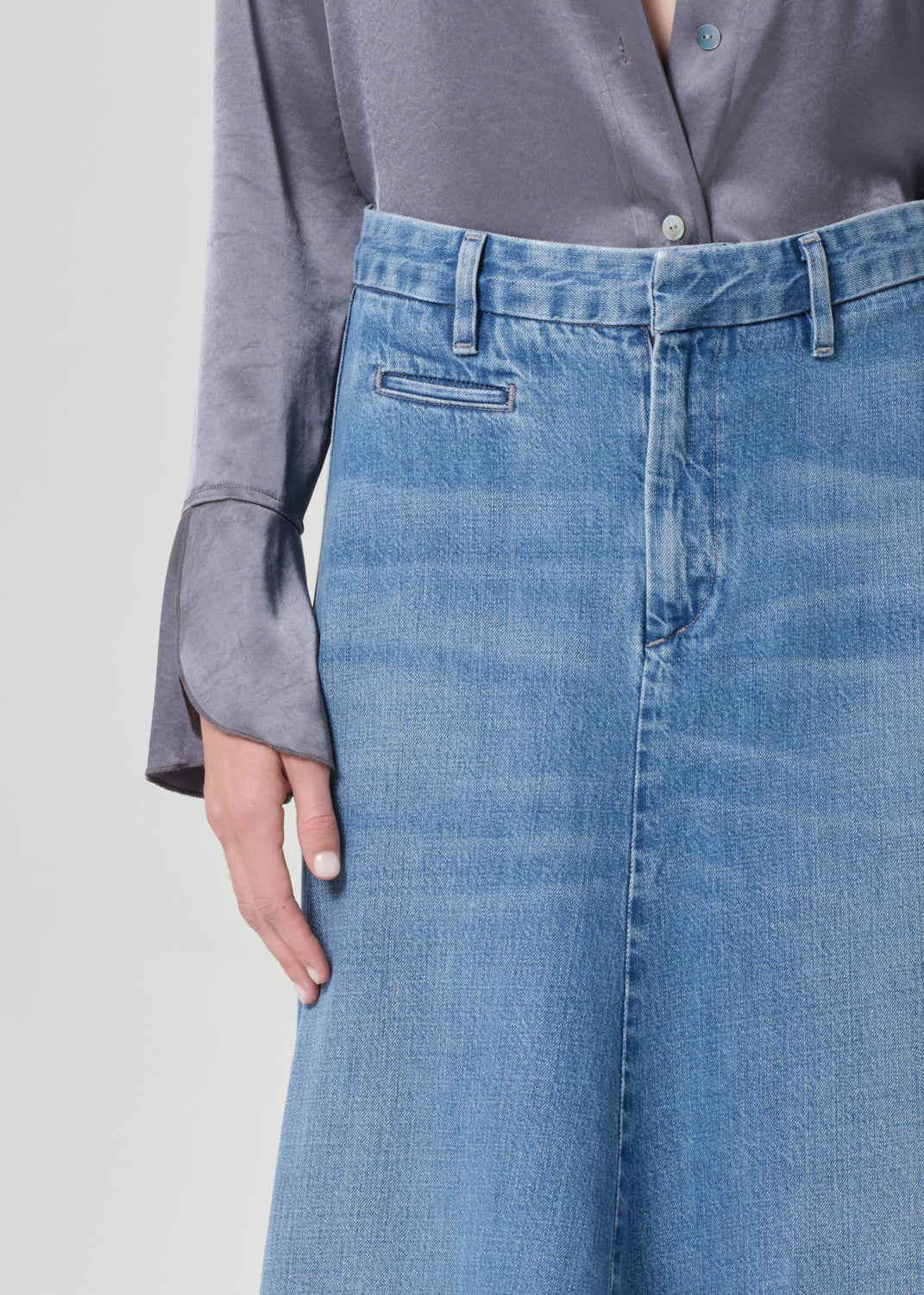 Person wearing a gray shirt and long blue denim skirt on a grey background