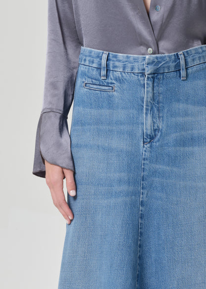 Person wearing a gray shirt and long blue denim skirt on a grey background