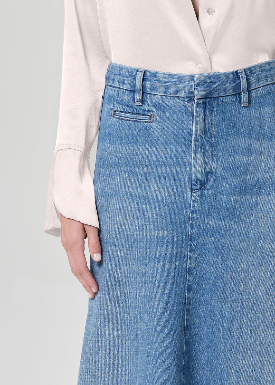 Person wearing a long denim skirt and light-colored blouse on a plain background