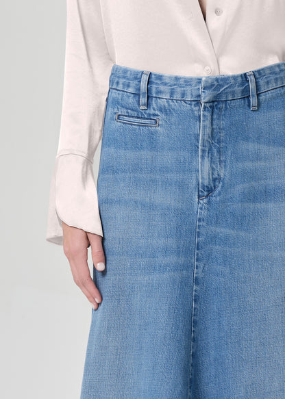 Person wearing a long denim skirt and light-colored blouse on a plain background