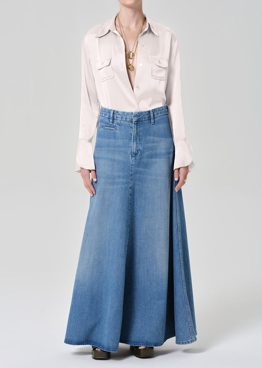 Person wearing a long denim skirt and light-colored blouse on a plain background