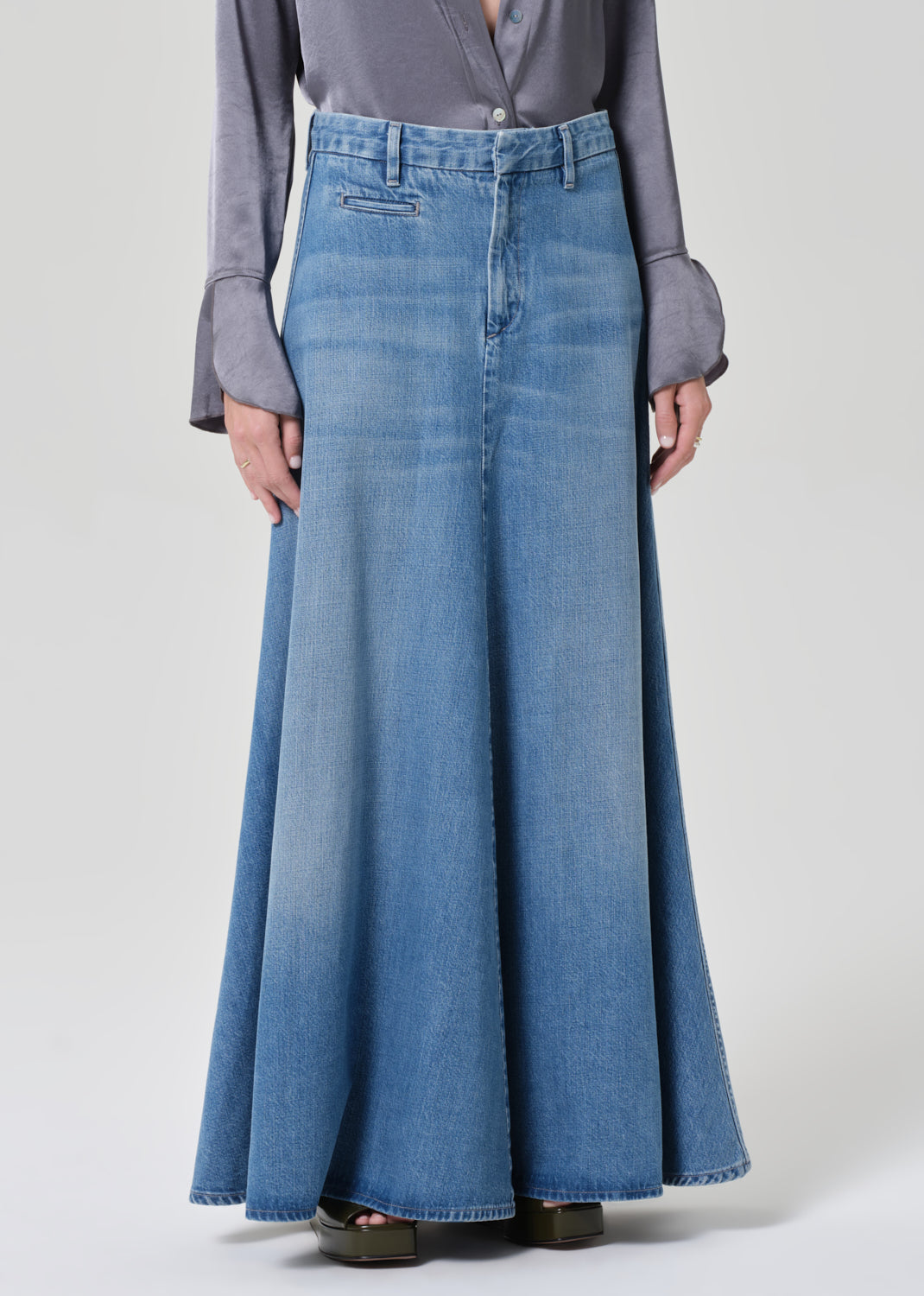 Person wearing a gray shirt and long blue denim skirt on a grey background