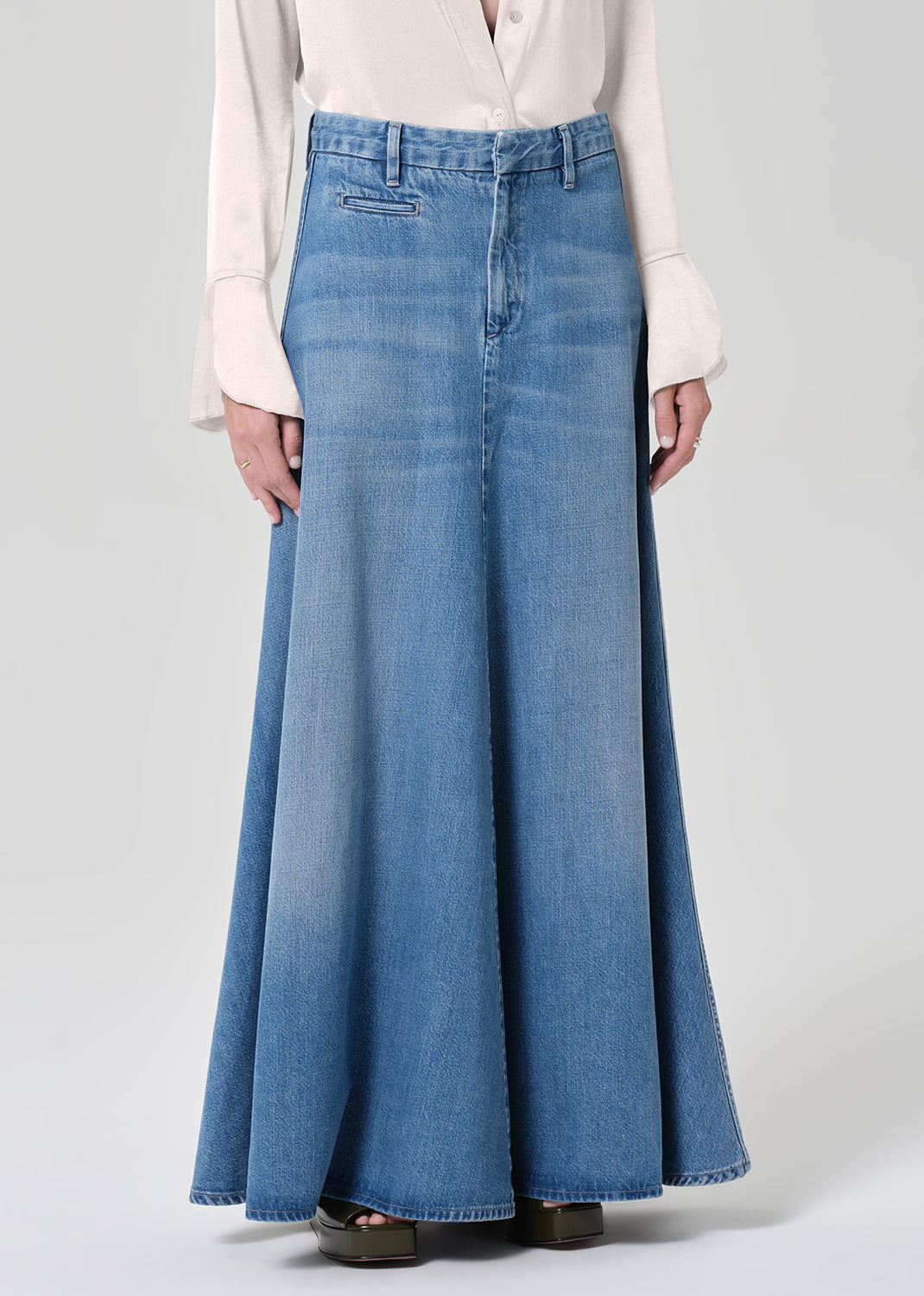 Person wearing a long denim skirt and light-colored blouse on a plain background
