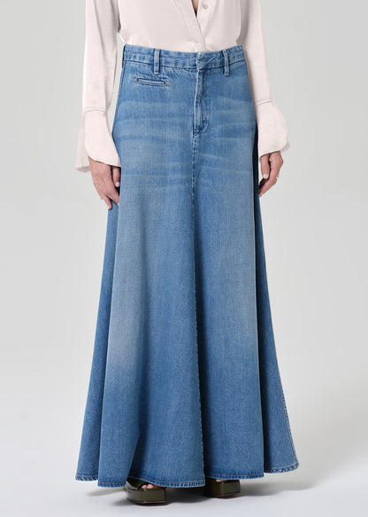 Person wearing a long denim skirt and light-colored blouse on a plain background