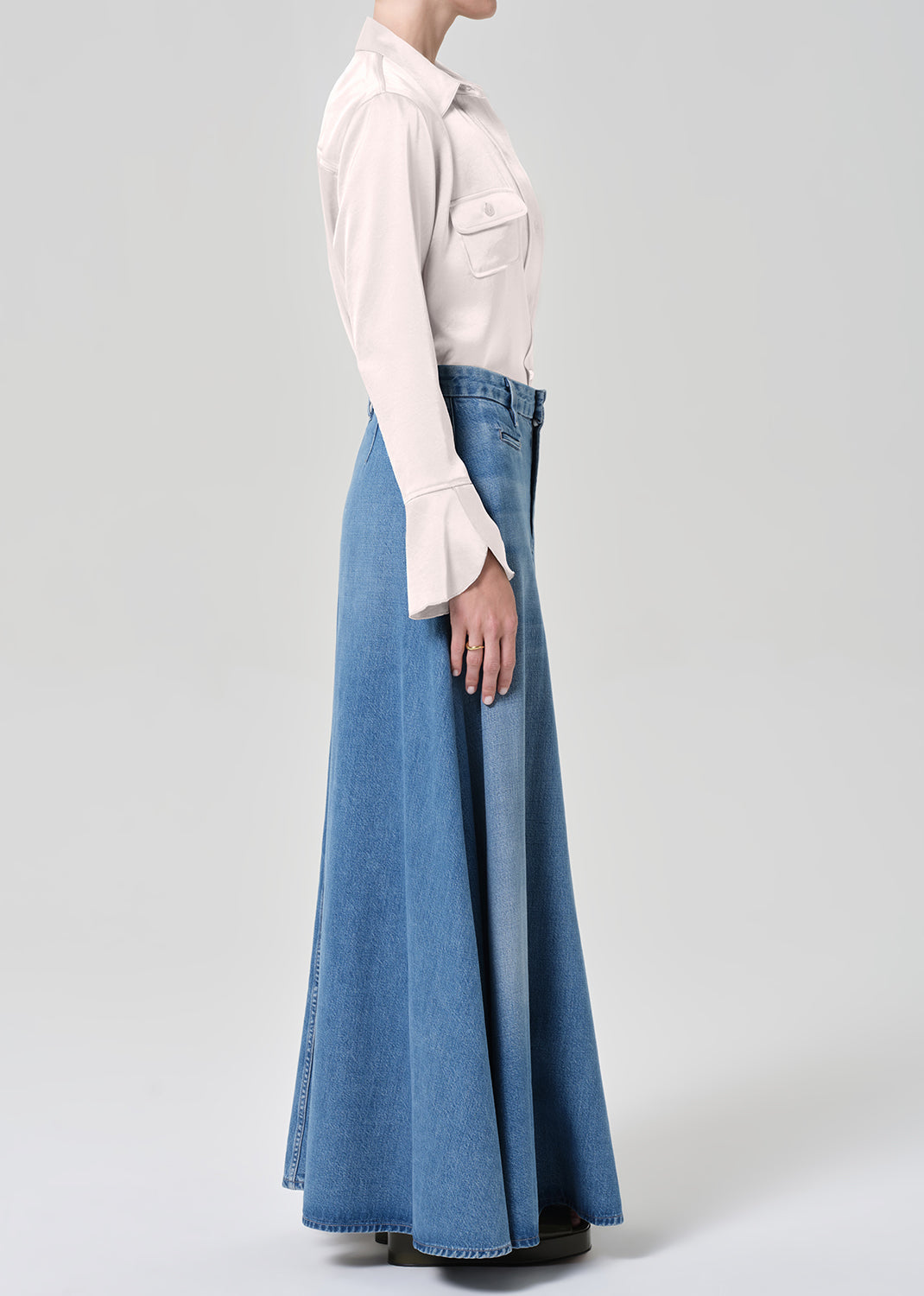 Person wearing a long denim skirt and light-colored blouse on a plain background