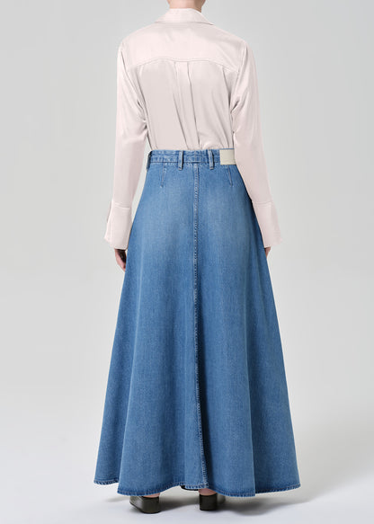 Person wearing a long denim skirt and light-colored blouse on a plain background