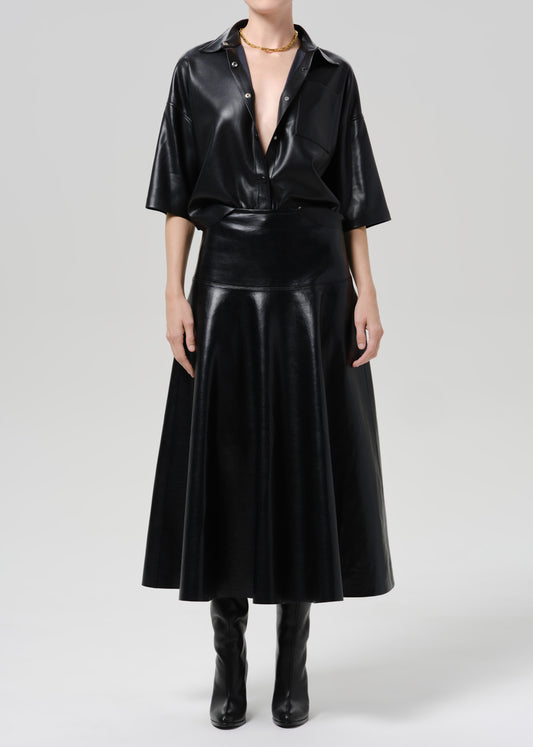 Person wearing a black leather short sleeve shirt with a black leather midi skirt on a grey background