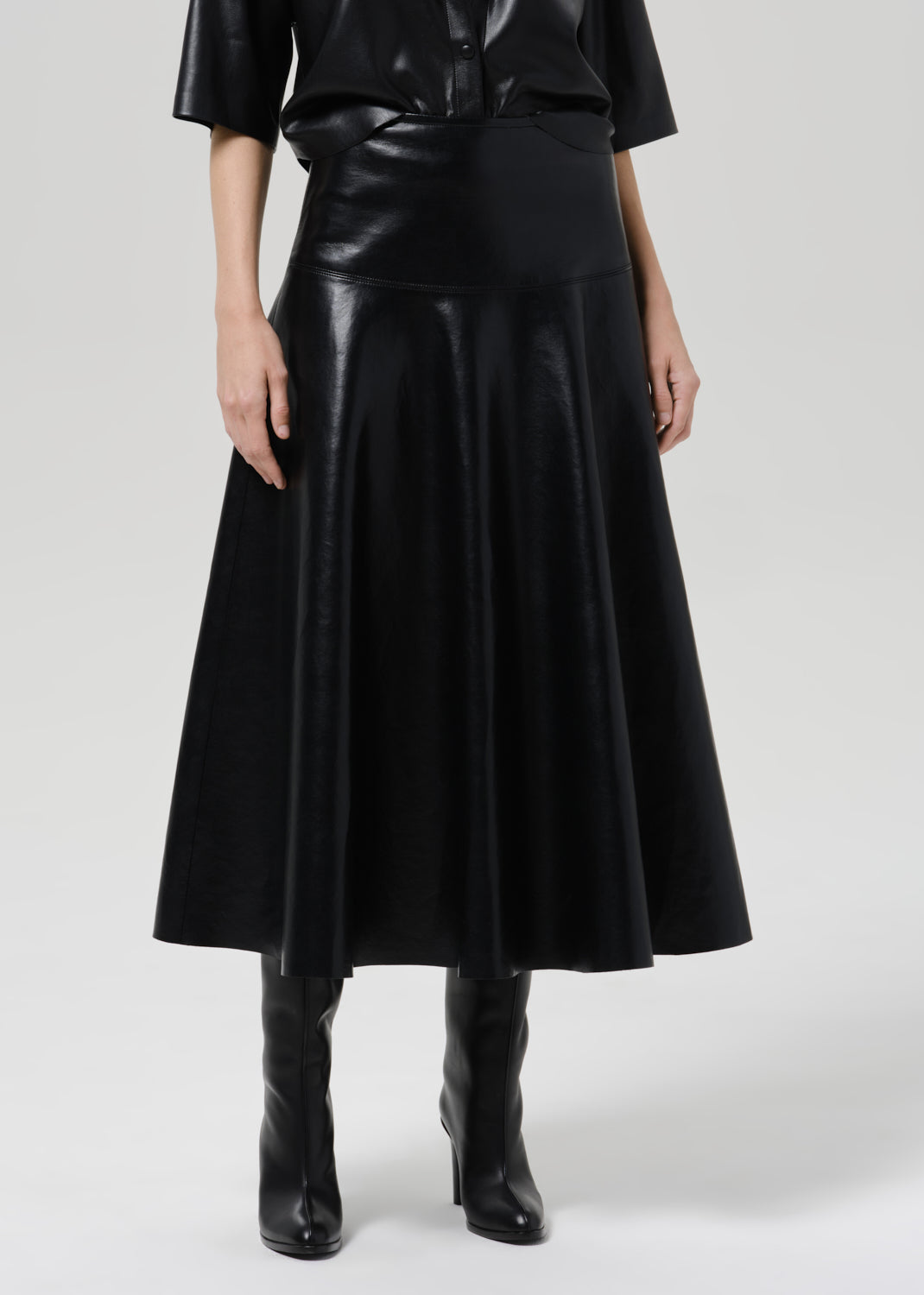 Person wearing a black leather short sleeve shirt with a black leather midi skirt on a grey background
