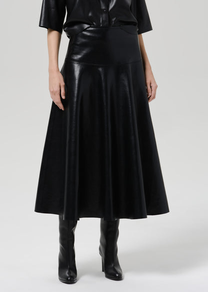 Person wearing a black leather short sleeve shirt with a black leather midi skirt on a grey background