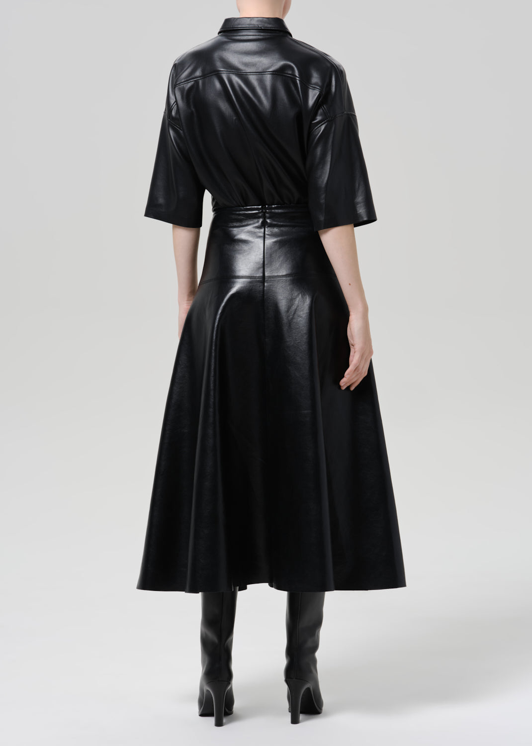 Person wearing a black leather short sleeve shirt with a black leather midi skirt on a grey background