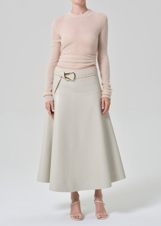Person wearing a light beige sweater and grey leather skirt with a belt