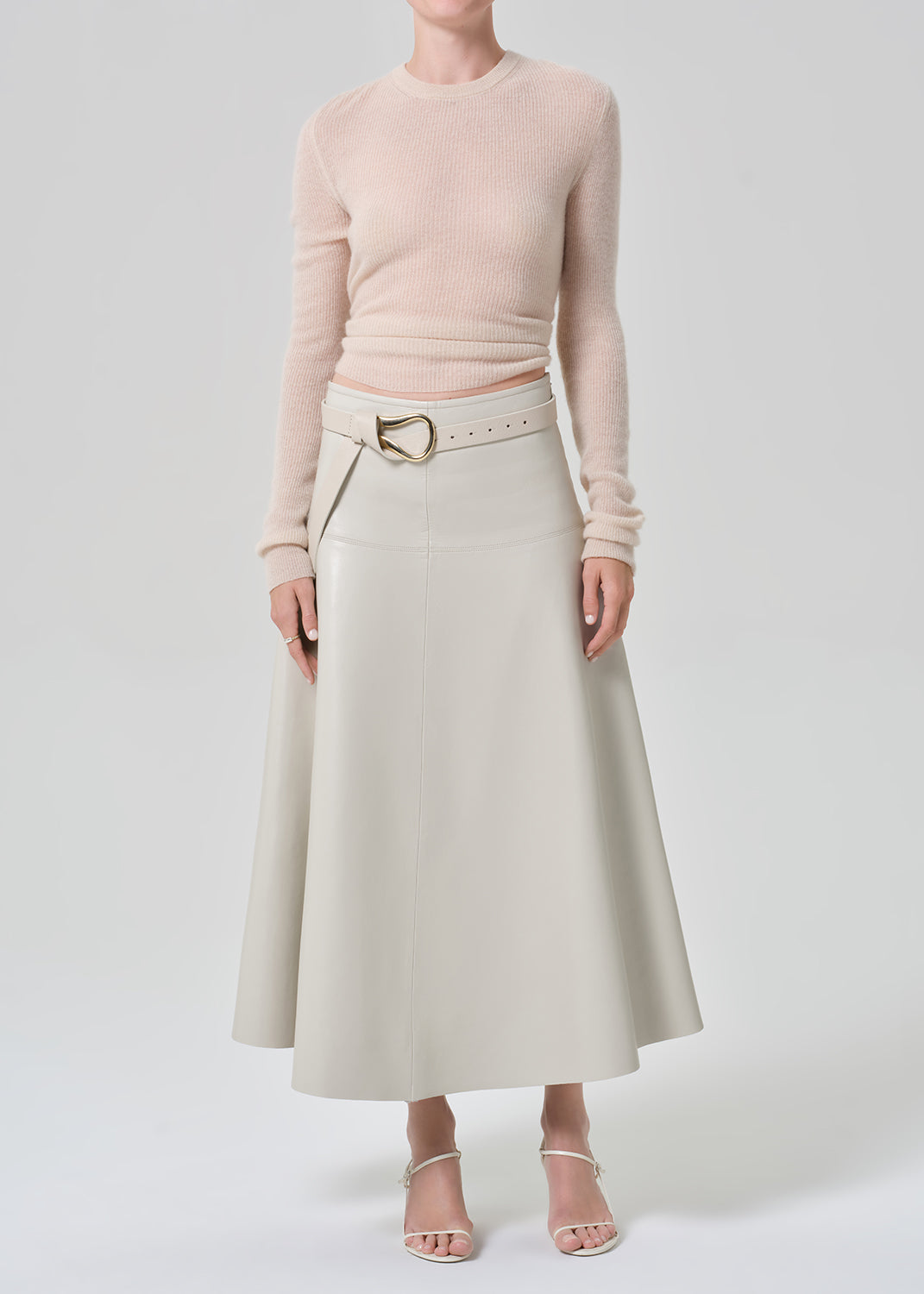 Person wearing a light pink sweater and light grey leathers skirt with a belt on a grey background