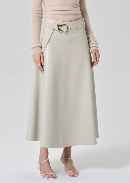 Person wearing a light pink sweater and light grey leathers skirt with a belt on a grey background