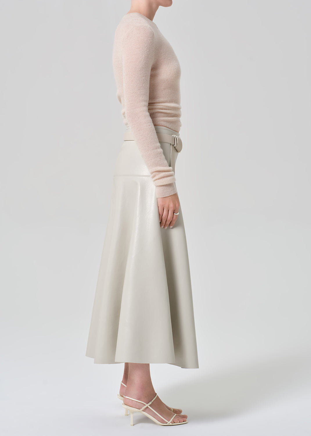 Person wearing a light pink sweater and light grey leathers skirt with a belt on a grey background