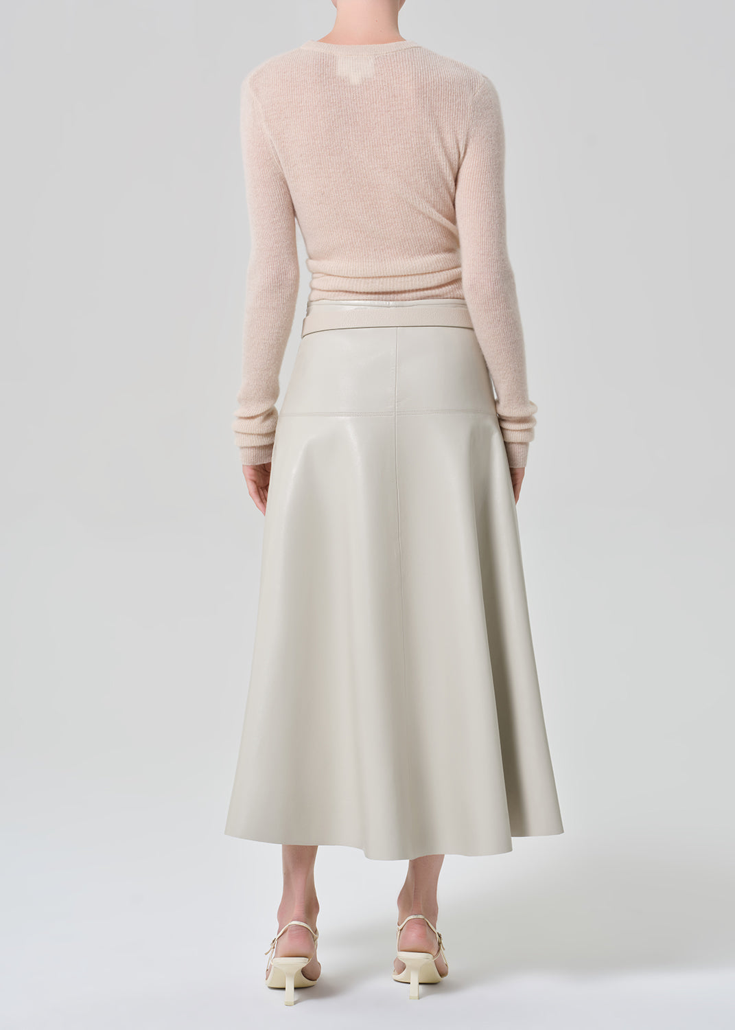 Person wearing a light pink sweater and light grey leathers skirt with a belt on a grey background