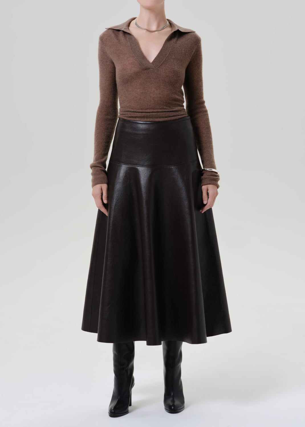 Person wearing a brown long sleeve collared knit top with a brown leather midi skirt on a grey background
