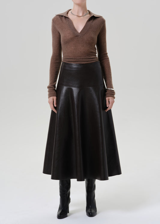 Person wearing a brown long sleeve collared knit top with a brown leather midi skirt on a grey background