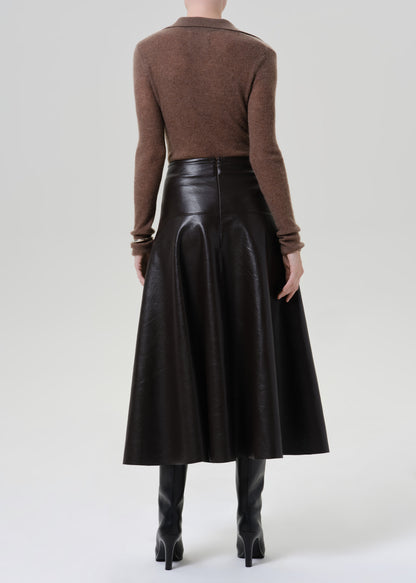 Person wearing a brown long sleeve collared knit top with a brown leather midi skirt viewed from the back on a grey background
