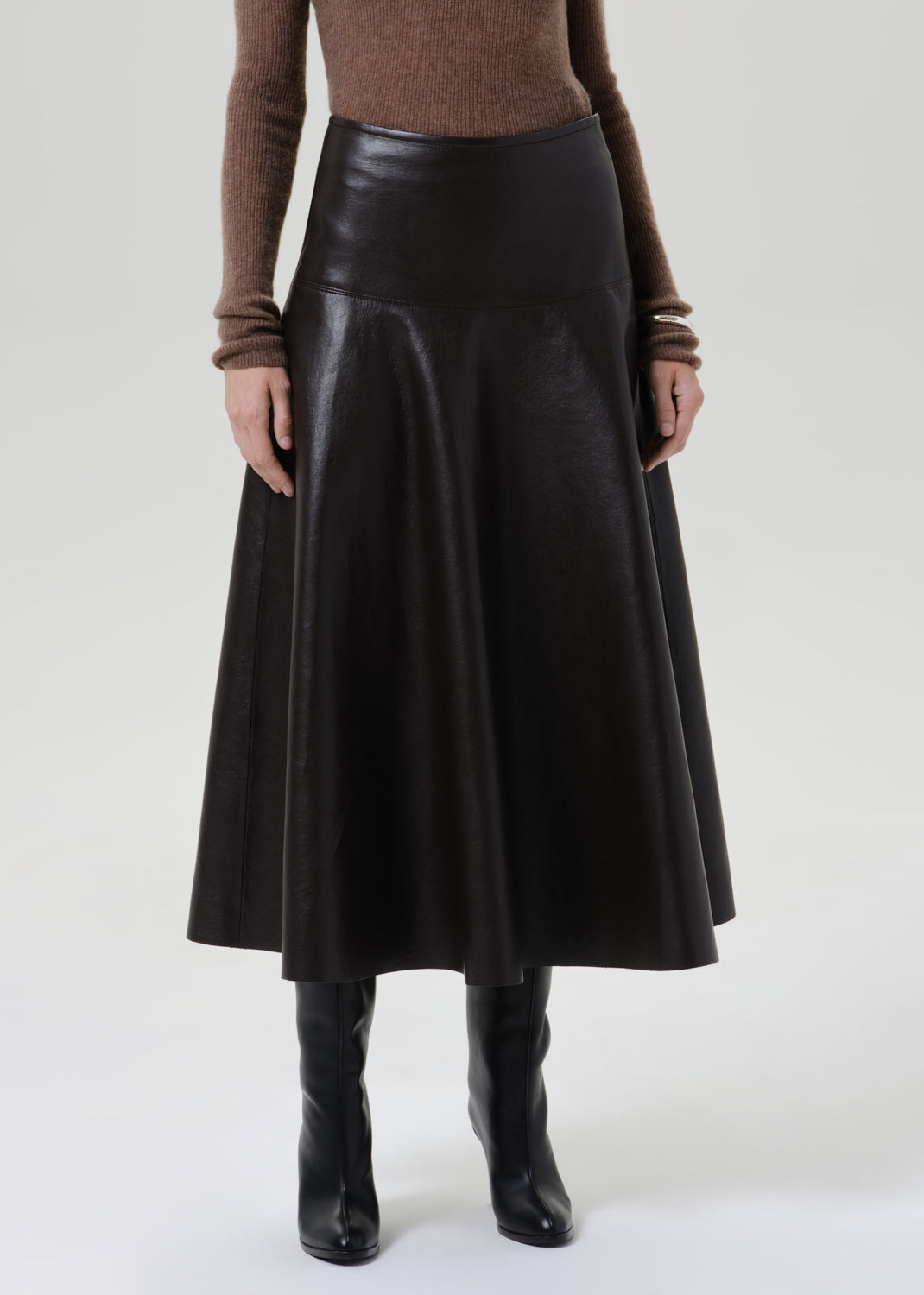 Person wearing a brown long sleeve collared knit top with a brown leather midi skirt on a grey background