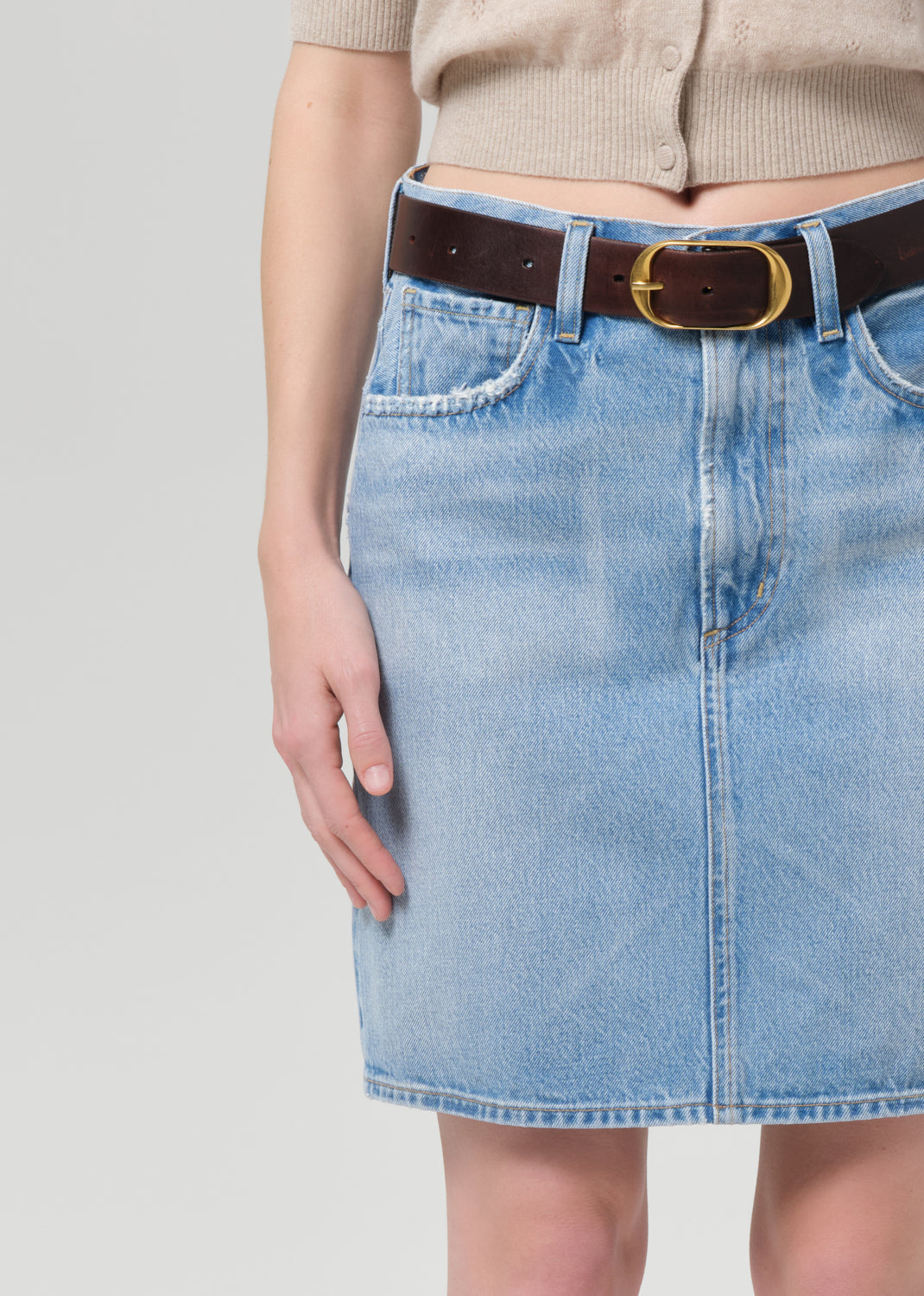 Person wearing a beige cardigan, blue denim skirt, and black sandals on a grey background