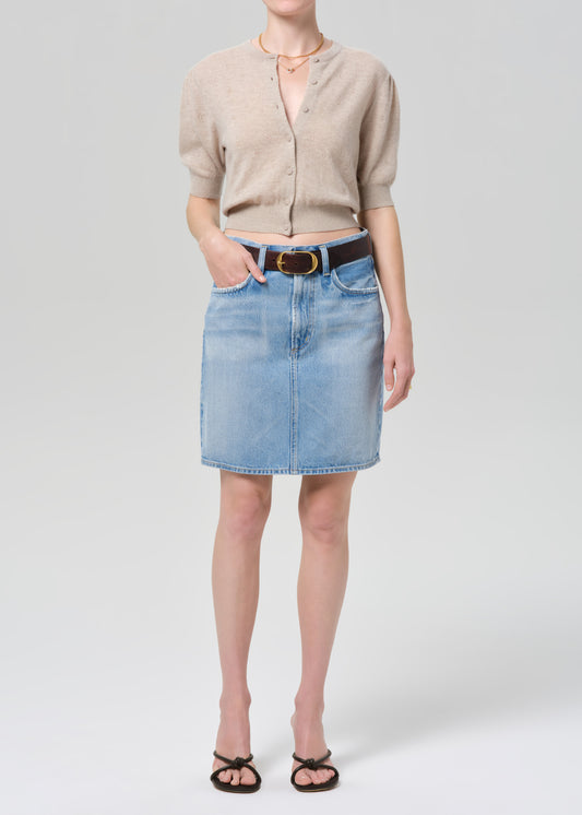 Person wearing a beige cardigan, blue denim skirt, and black sandals on a grey background