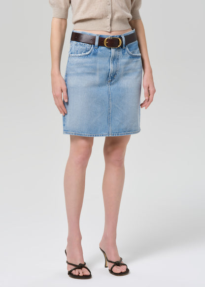Person wearing a beige cardigan, blue denim skirt, and black sandals on a grey background