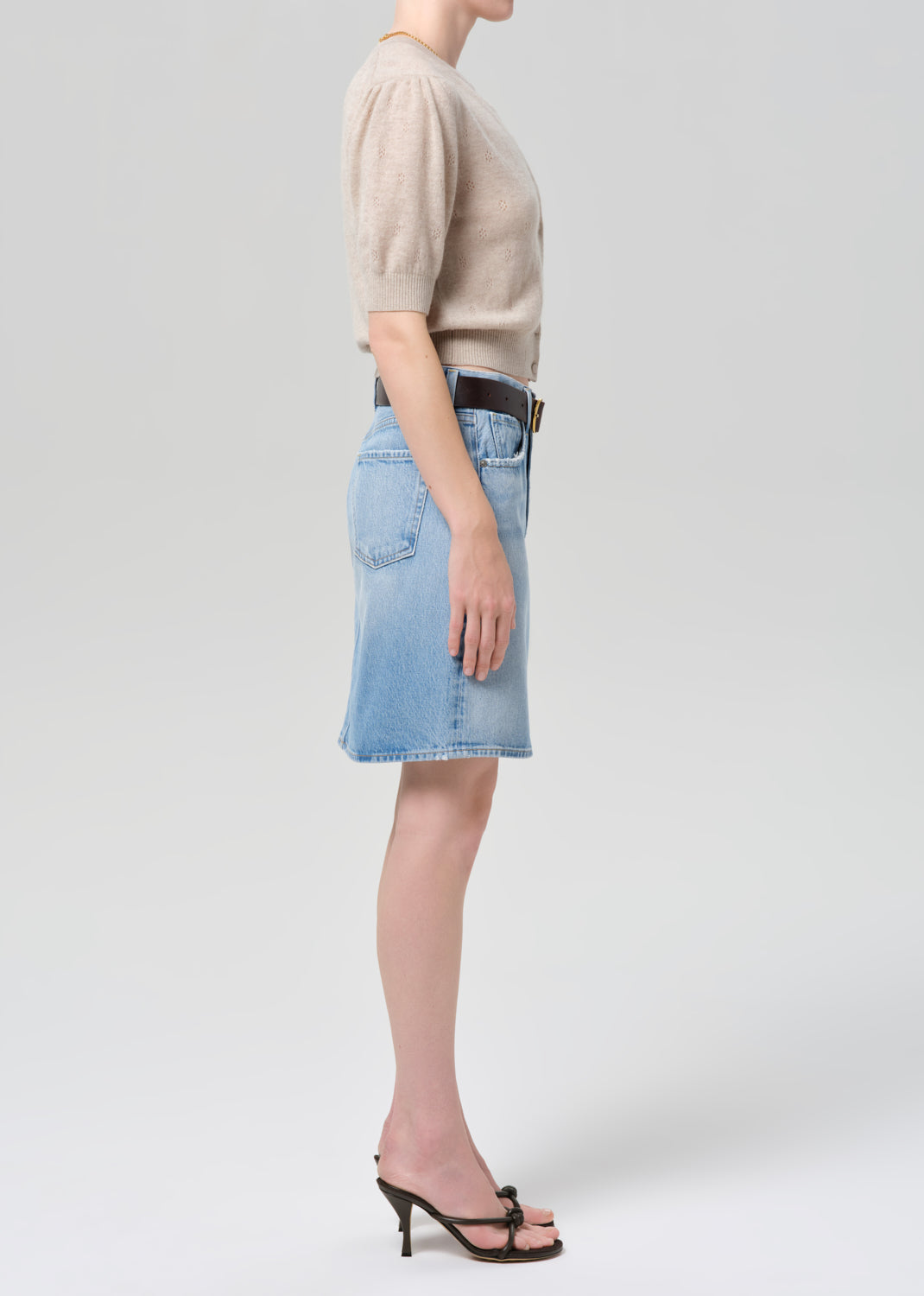 Person wearing a beige cardigan, blue denim skirt, and black sandals on a grey background