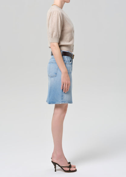 Person wearing a beige cardigan, blue denim skirt, and black sandals on a grey background