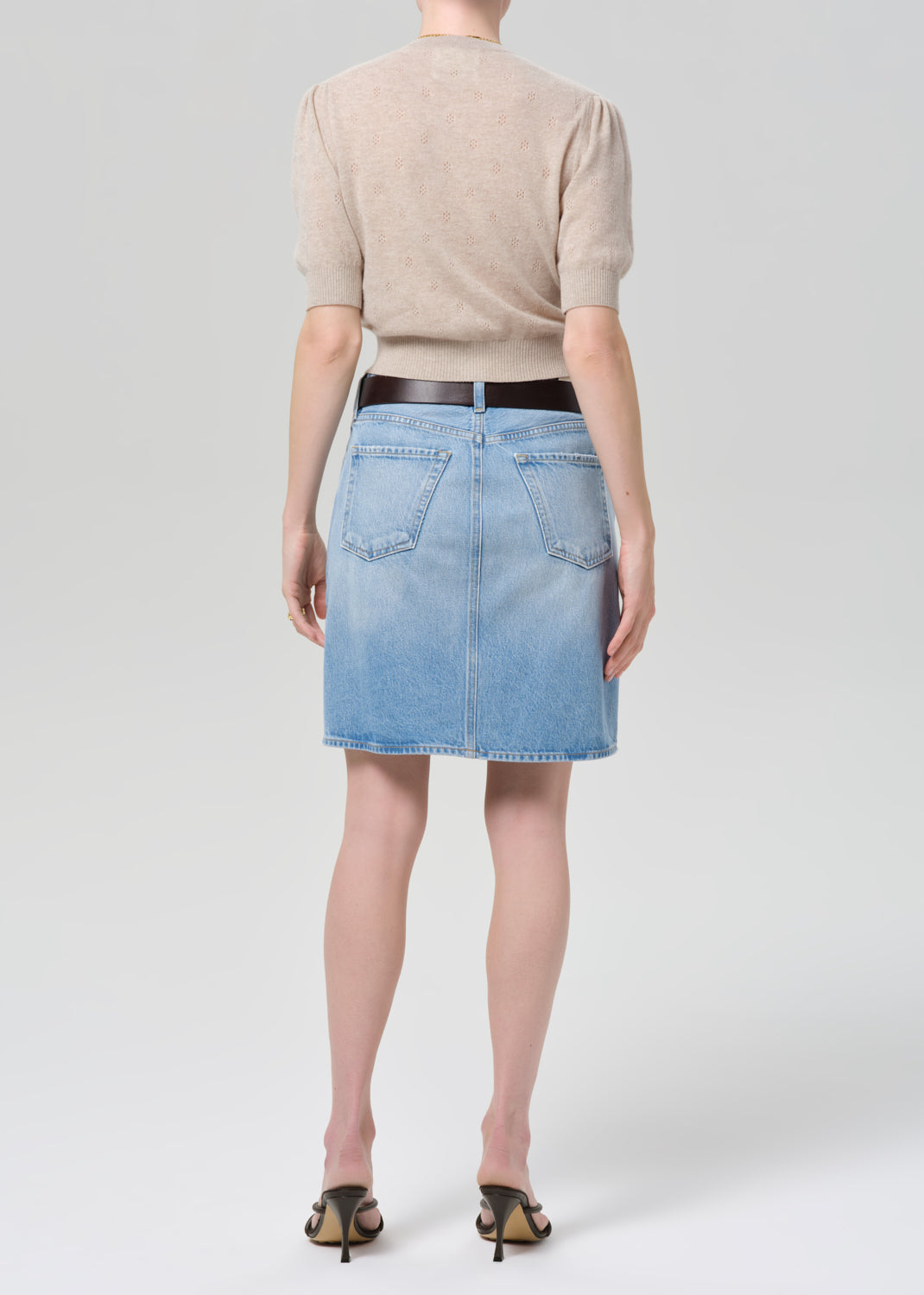 Person wearing a beige cardigan, blue denim skirt, and black sandals on a grey background