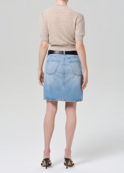 Person wearing a beige cardigan, blue denim skirt, and black sandals on a grey background