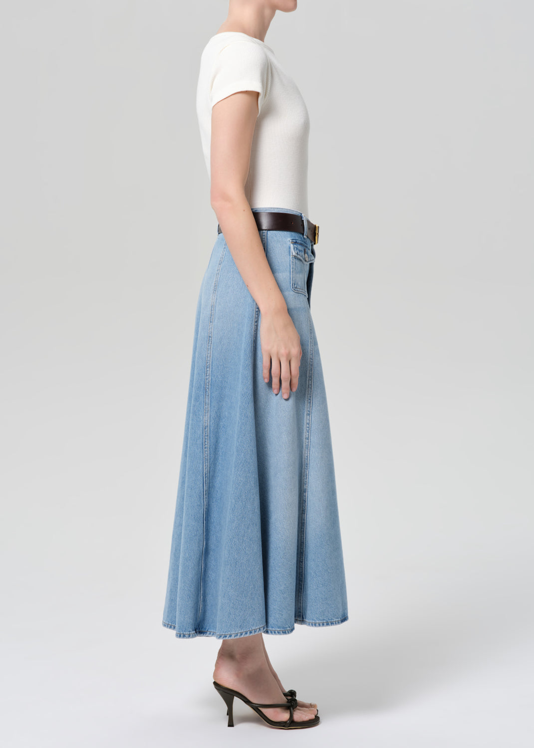 Person wearing a white top and light blue denim skirt on a plain background