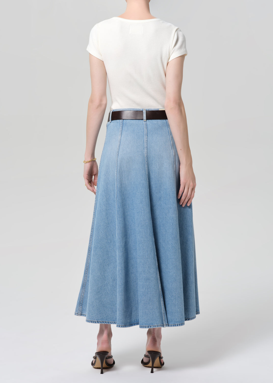 Person wearing a white top and blue denim skirt on a plain background