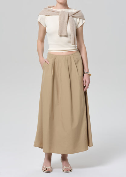 Woman wearing a beige top and long skirt on a grey background