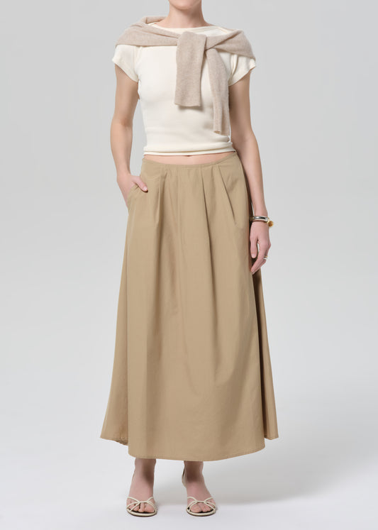 Woman wearing a beige top and long skirt on a grey background