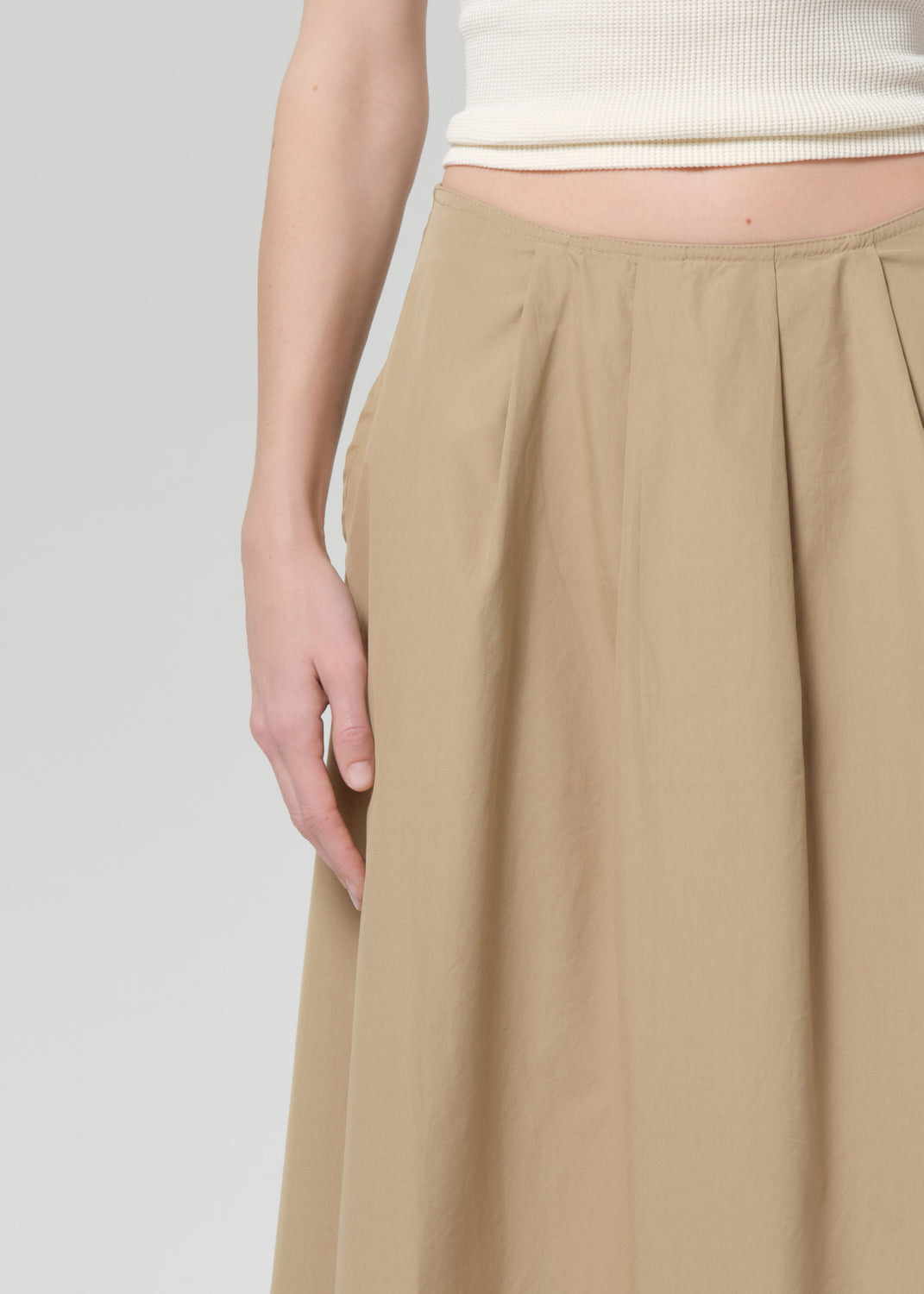 Woman wearing a beige top and long skirt on a grey background